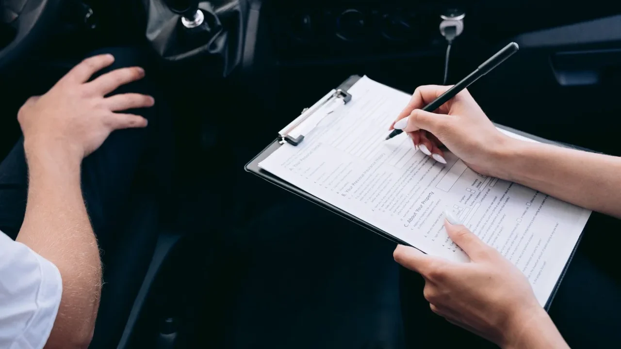 Persoana completand un formular pe clipboard, in interiorul unei masini